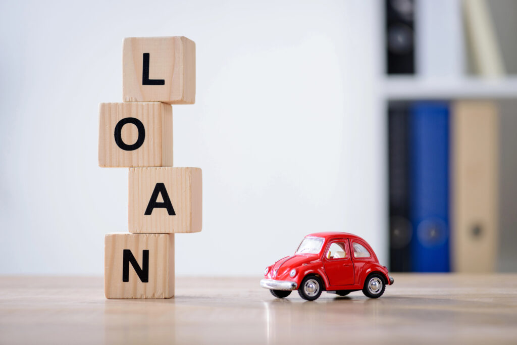 A red car next to blocks spelling 'LOAN,' representing the financial burden of 7-year car loans.