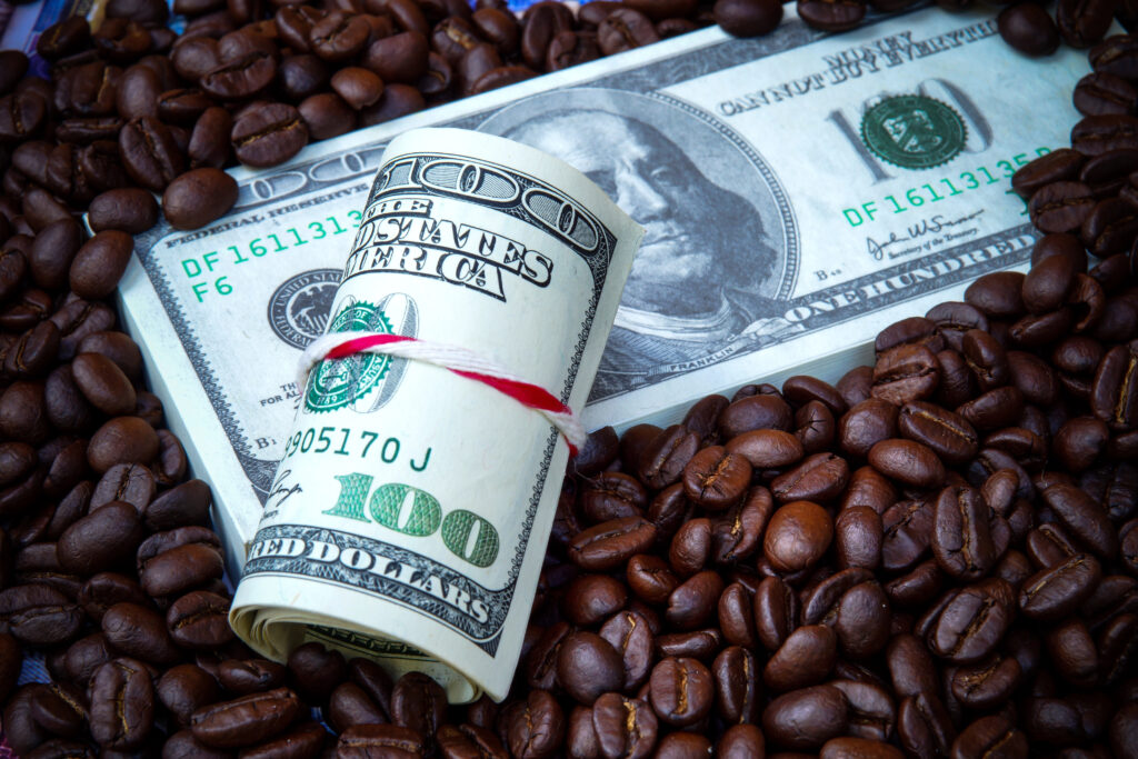 Rolled-up U.S. dollar bills sitting on coffee beans, symbolizing the Latte Factor myth about small spending and wealth building.