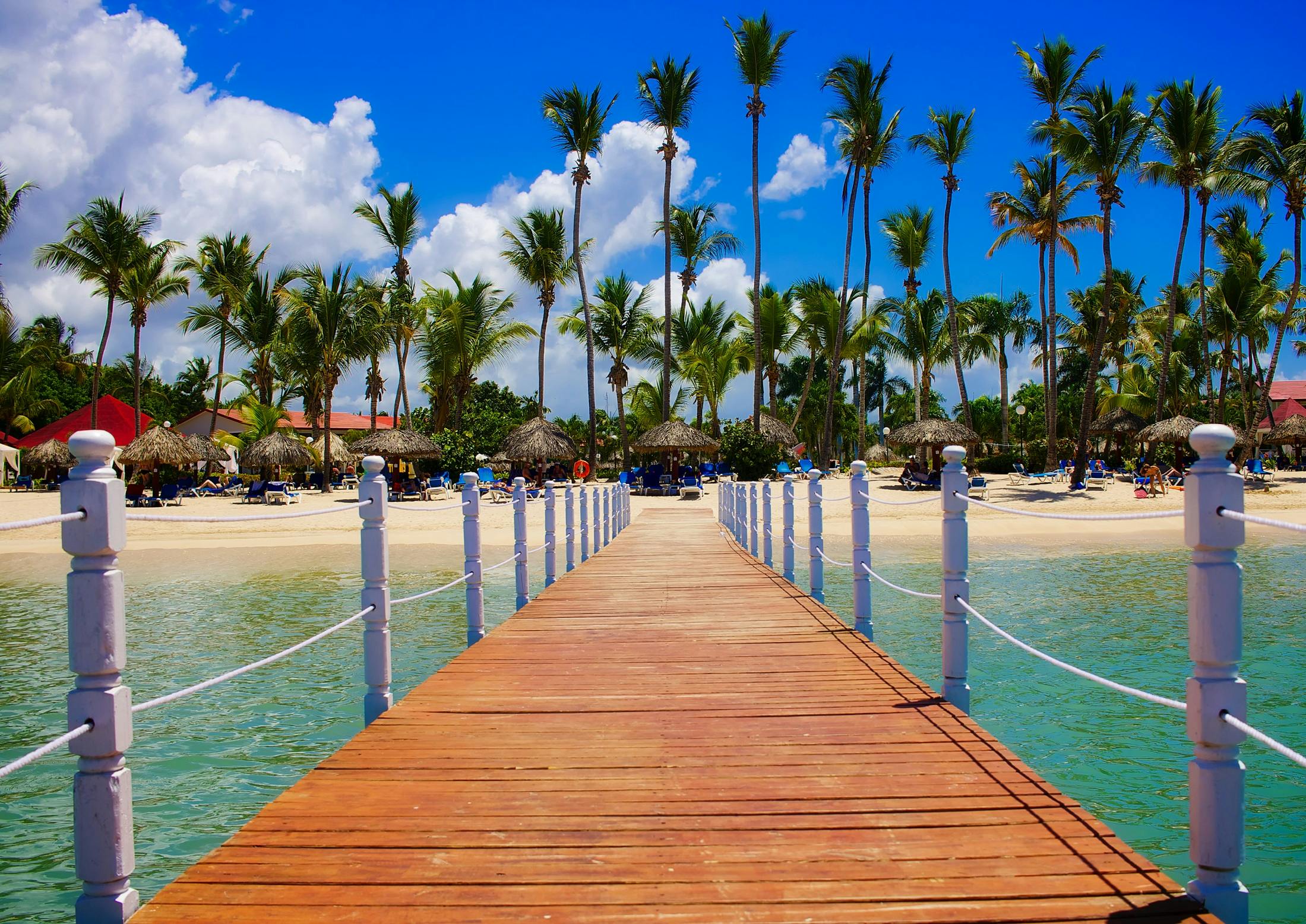 Wooden dock leading to a tropical beach resort with palm trees and clear blue waters.. Best Personal Finance Blog for Investing & Retirement